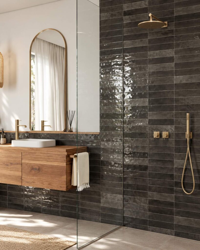 Badkamer met Mindelo Glans Nairobi Slate 5x30 wandtegels, een houten wastafelmeubel en messing douchekranen